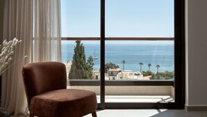 A room with a large window offering a view of the sea and buildings.