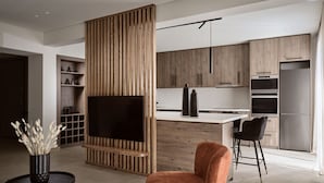 A modern kitchen with wooden cabinets, a large flat-screen TV, and a dining area with a bar stool.