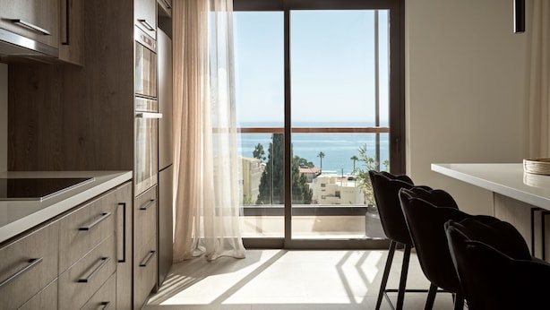 A modern kitchen with a large window overlooking a cityscape and the sea.