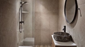 A modern bathroom with a shower, a round mirror, and a stone basin.