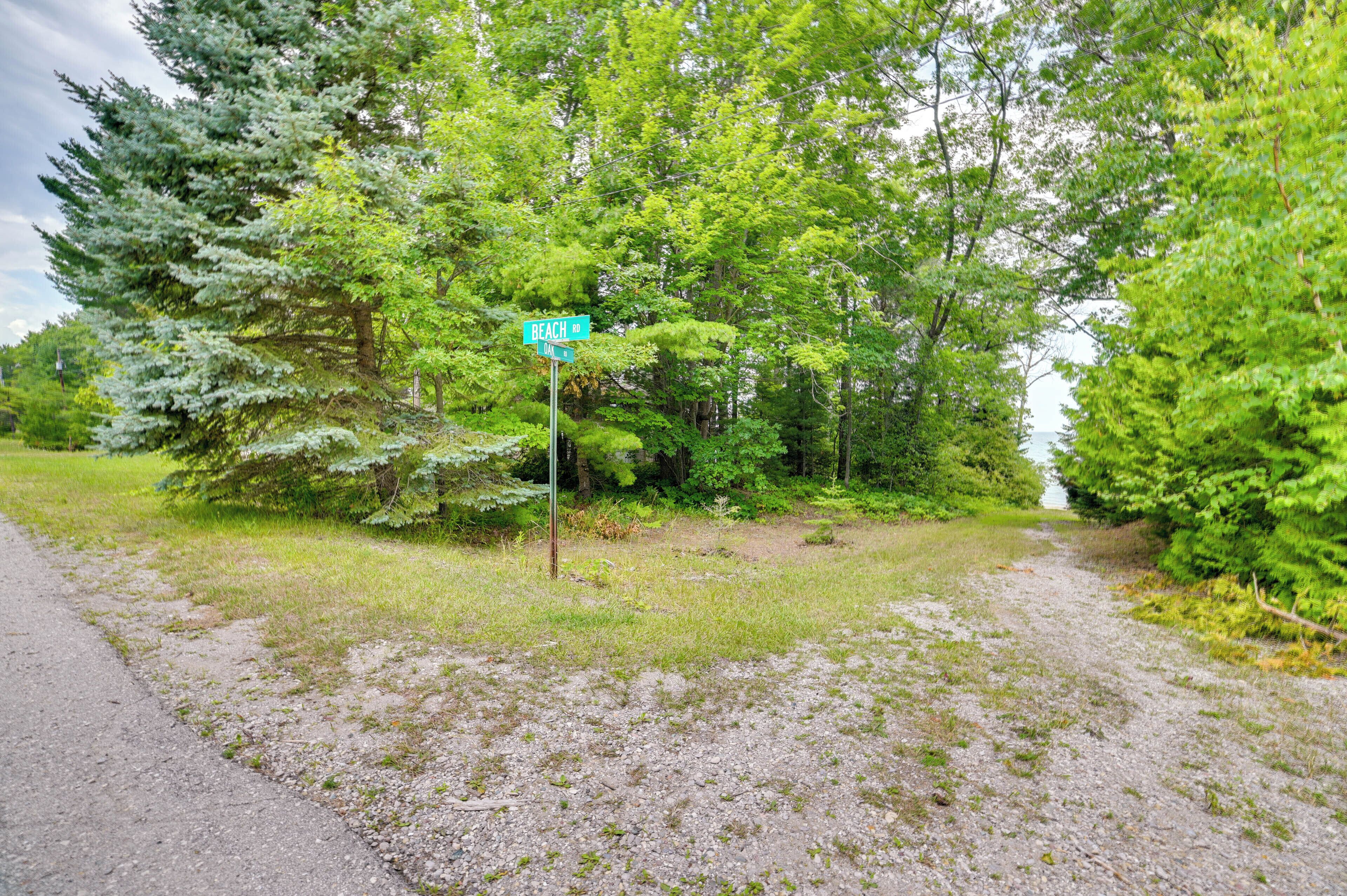 A gravel path leading to a beach sign amidst dense greenery.