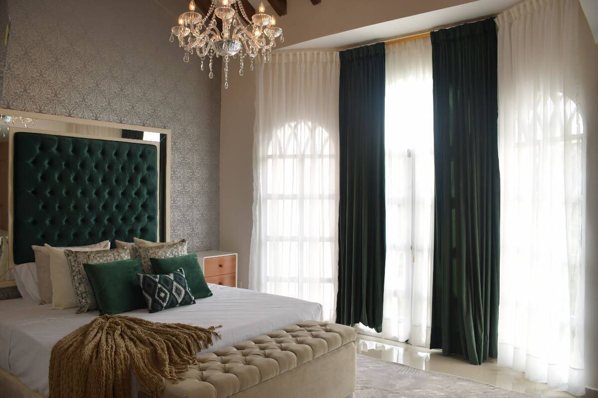 Une chambre à coucher avec une tête de lit capitonnée, un grand lit avec de nombreux oreillers, un banc au pied du lit et un lustre.