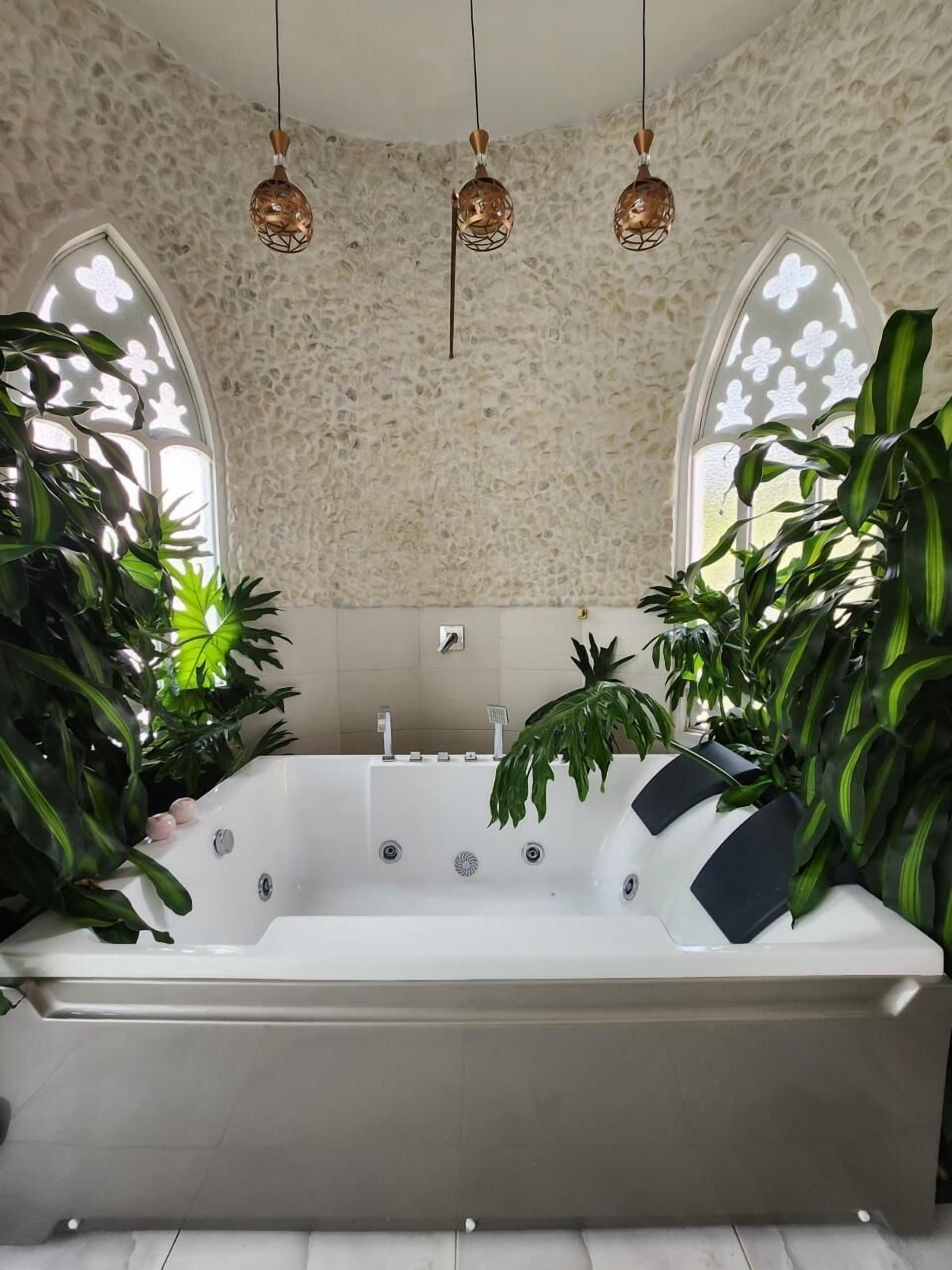 Un baño moderno con una bañera independiente, paredes con textura de piedra y ventanas amplias con paneles de vidrio decorativos.