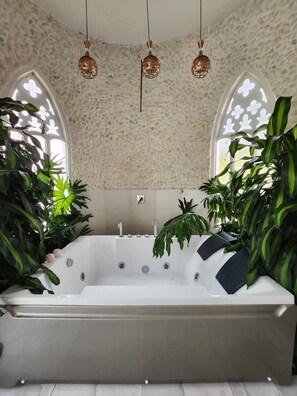 Un baño moderno con una bañera independiente, paredes con textura de piedra y ventanas amplias con paneles de vidrio decorativos.