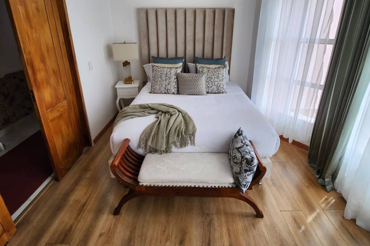 Une chambre avec un grand lit, un plancher en bois, un tableau au-dessus du lit et une porte en bois sur le côté gauche.