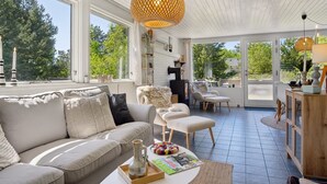 Amplia sala de estar con un sofá grande, una mesa de centro y una chimenea. Varias ventanas ofrecen luz natural y vistas al exterior.