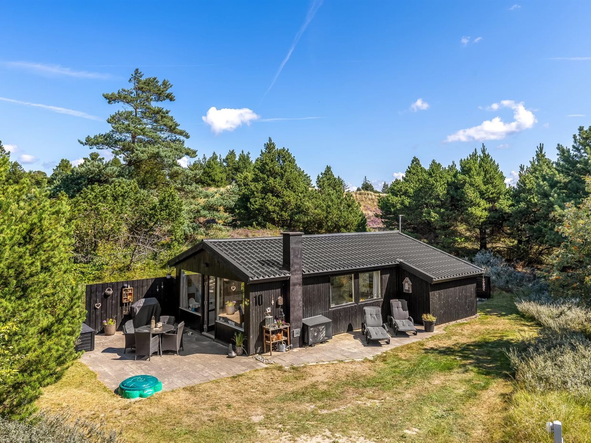 A modern wooden cabin with a patio area, outdoor seating, and a view of the surrounding forest.