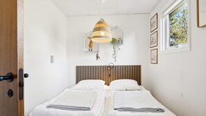 Habitación con dos camas, una lámpara colgante y una ventana con vista a árboles.