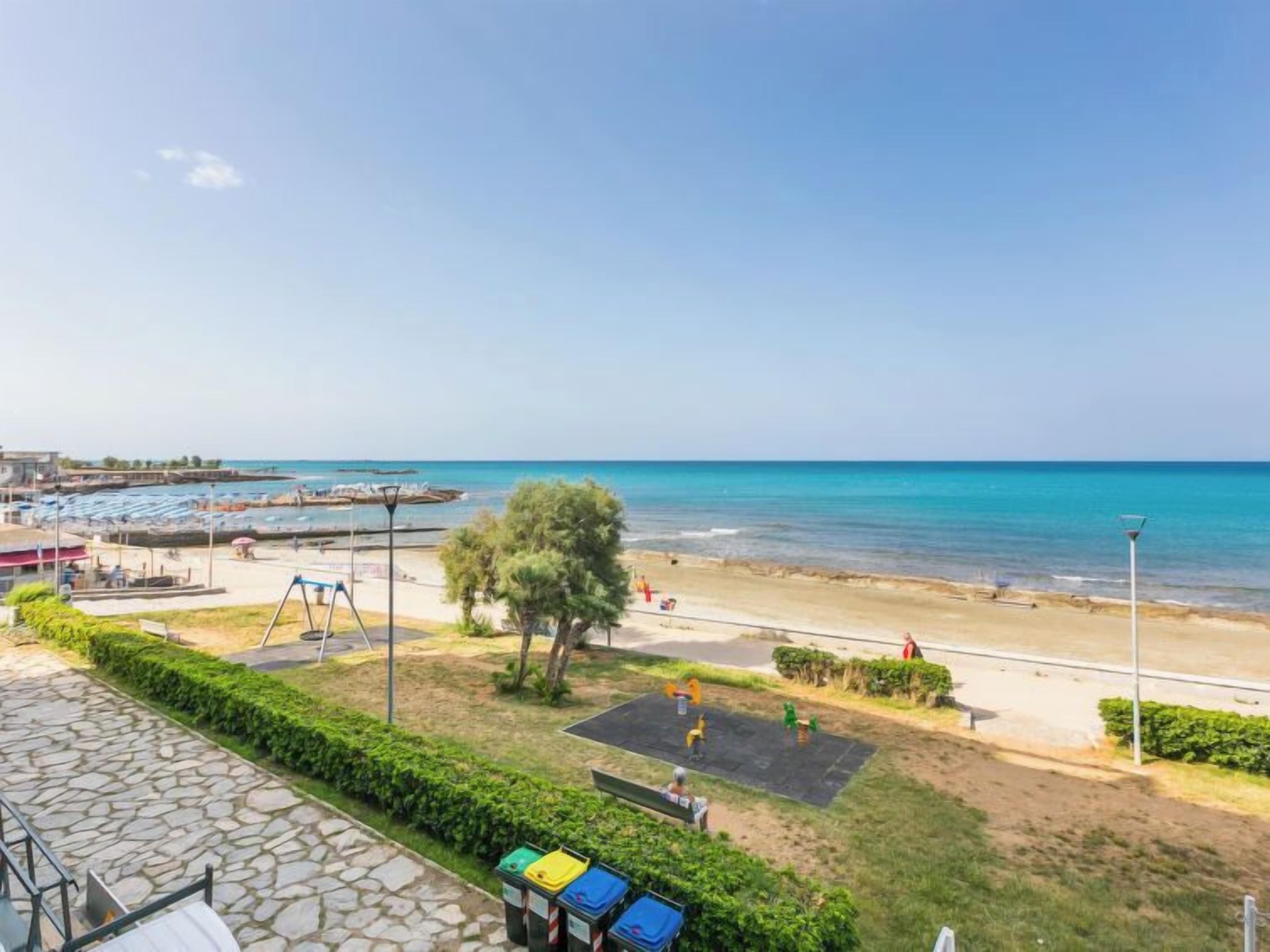 A beach view with a playground, a stone pathway, and a row of colorful bins.