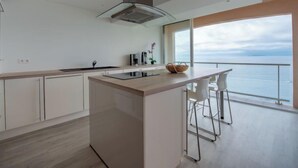 A modern kitchen with a central island, white cabinetry, and a view of the sea through large windows. - Le Grand Large by Interhome (Cavalaire)