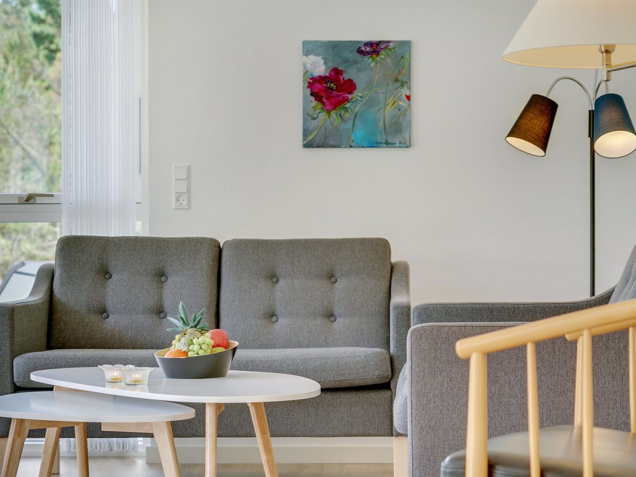 A modern living room with grey upholstered sofas, a round white table with a fruit bowl, and a floor lamp.