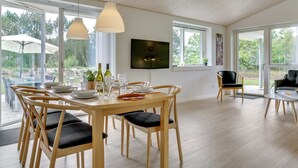 A dining area with a wooden table and chairs, a TV mounted on the wall, and large windows offering a view of the outdoors. - "Alona" - 250m from the sea by Interhome (Jerup)