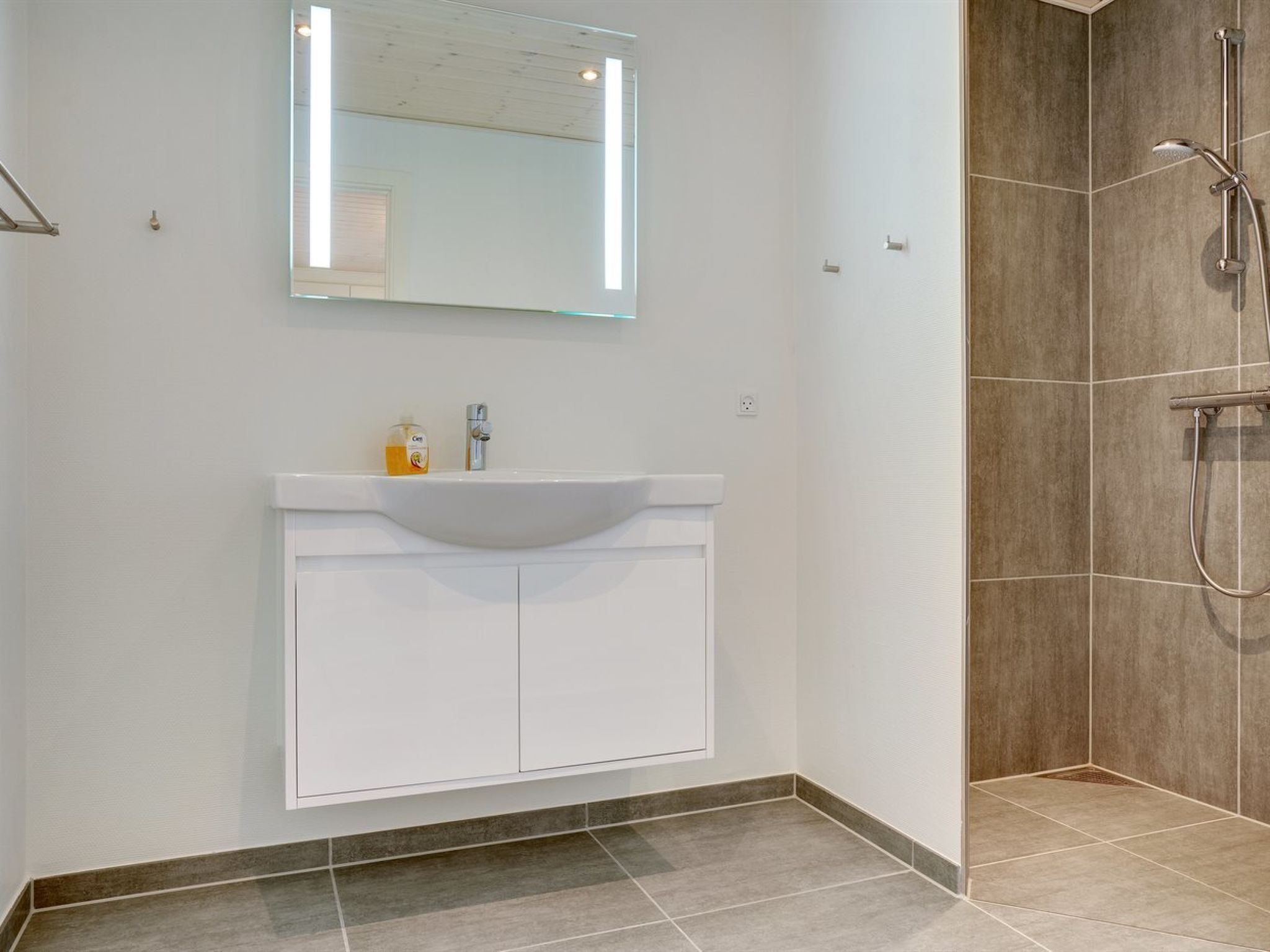 Une salle de bain moderne avec un meuble-lavabo blanc, un grand miroir et un espace douche.