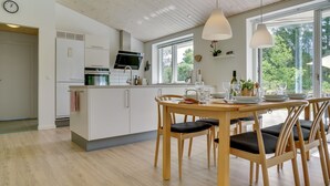 A modern kitchen with white cabinetry, a built-in oven, and a dining area with wooden chairs and a table set for four. - "Alona" - 250m from the sea by Interhome (Jerup)