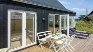 A modern house with a dark exterior, large sliding glass doors, and a wooden deck with outdoor furniture. - "Helga" - 800m from the sea by Interhome (Skagen)