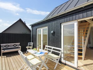 Een houten terras met een tafel en stoelen, een schuifpui en een overdekt gedeelte met een ladder.