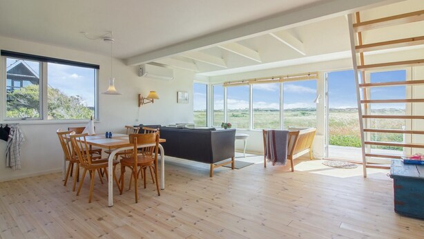 A spacious room with a wooden floor, a dining area with chairs and a table, a black sofa, and large windows offering a view of the outdoors. - "Helga" - 800m from the sea by Interhome (Skagen)