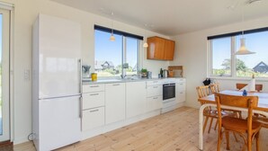 A modern kitchen with white cabinets, a built-in oven, and a dining area with wooden chairs and a table. - "Helga" - 800m from the sea by Interhome (Skagen)