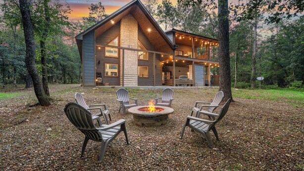 A lodge with a stone fireplace, outdoor seating, and a view of the forest.