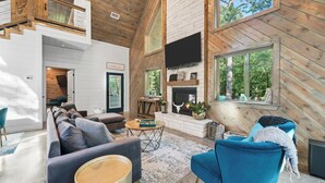 A spacious living area with a large sofa, a blue armchair, and a fireplace. A wooden staircase leads to an upper level.
