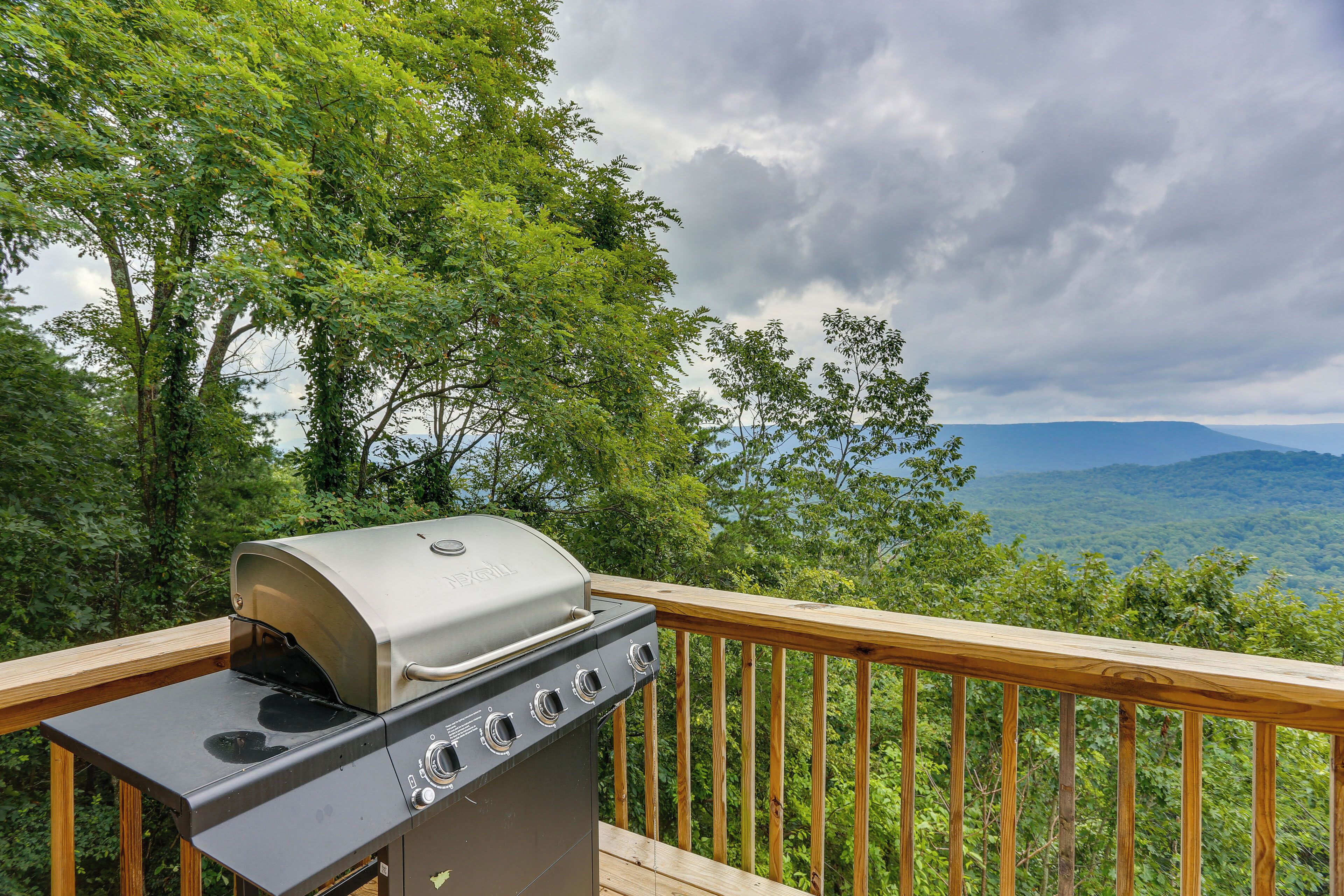 Una parrilla de barbacoa en una terraza de madera con vistas a un bosque y montañas.