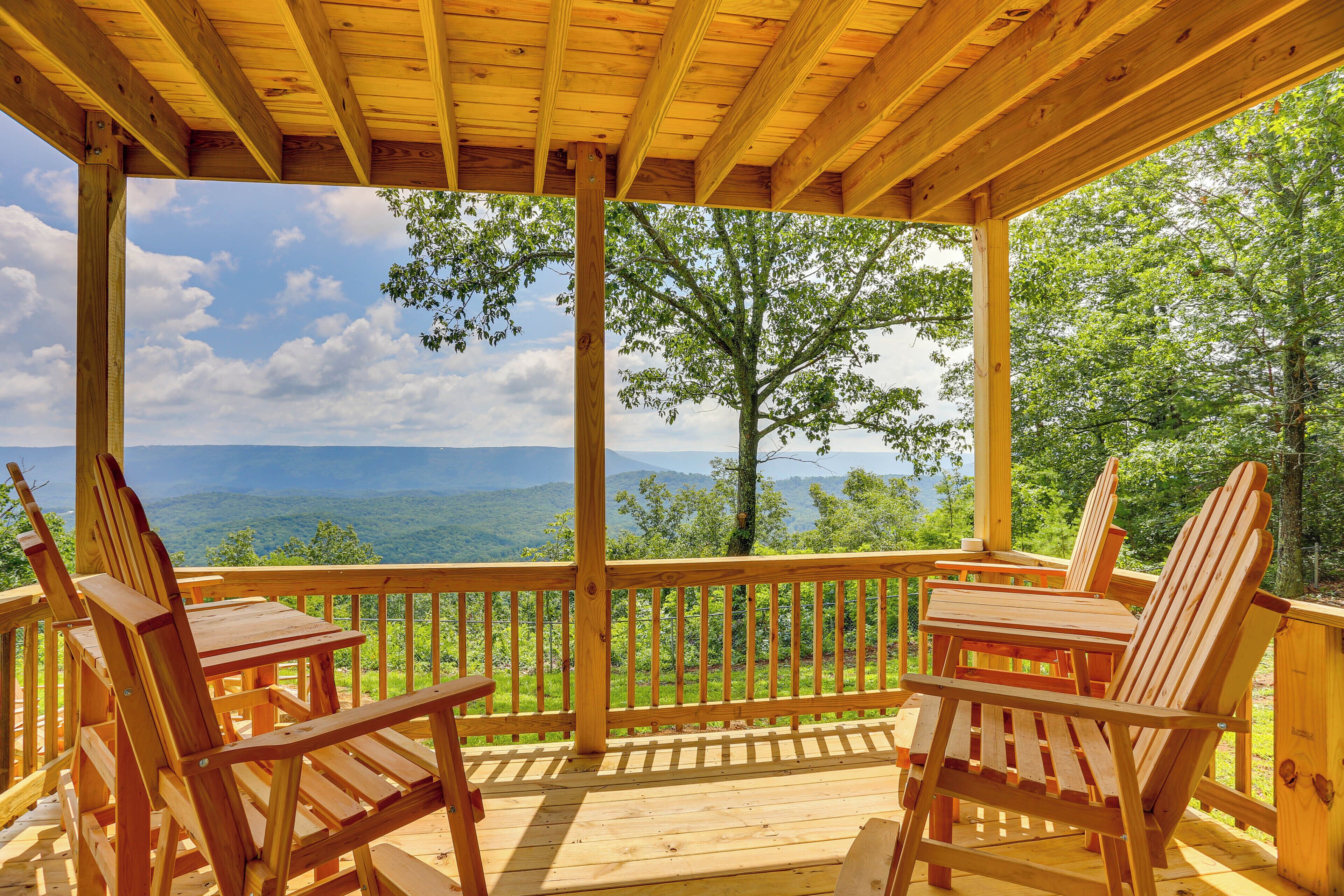 A wooden deck with Adirondack chairs and a view of mountains.