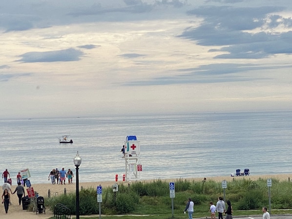 A beach with a lifeguard tower, a boat, and people walking along the shore.