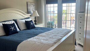 A bedroom with a bed, a nightstand, a lamp, a dresser, and a window with a view.