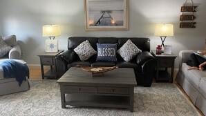 A living room with a black leather sofa, two side tables with lamps, a coffee table, and a framed picture on the wall.