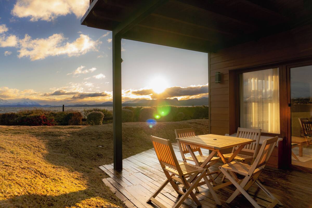 Una terraza de madera con una mesa y sillas, con vistas a un paisaje pintoresco al atardecer.