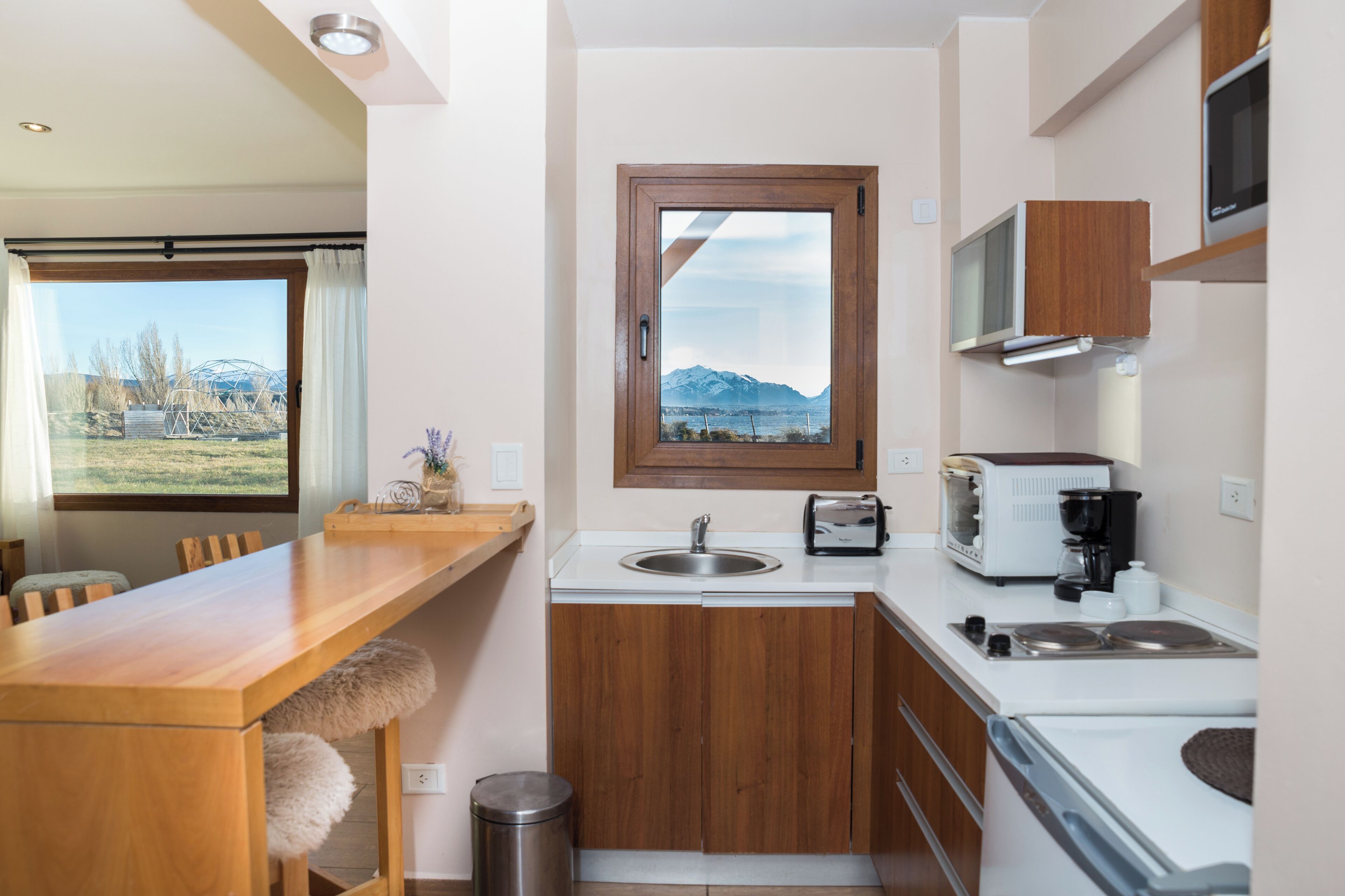 A compact kitchen with wooden cabinets, a built-in microwave, a sink, and a window with a mountain view.
