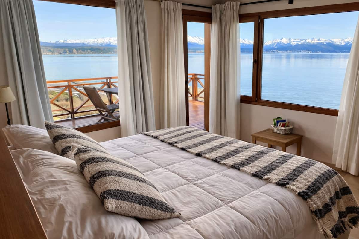 Un dormitorio con una cama grande, vistas a un lago y montañas al fondo.