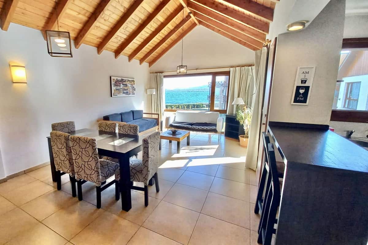 Un área de comedor con una mesa y sillas, un sofá y vista al mar.