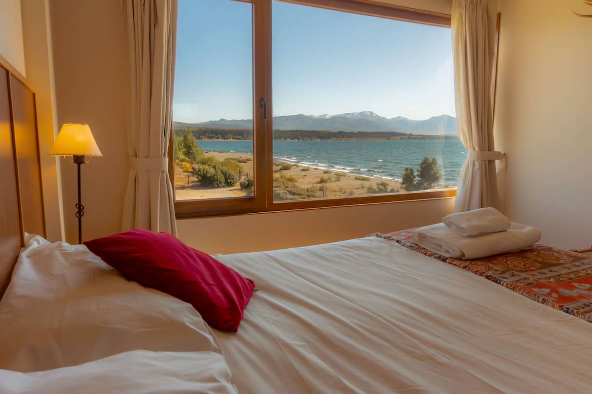 Un dormitorio con un amplio ventanal que ofrece vistas a un lago y montañas.