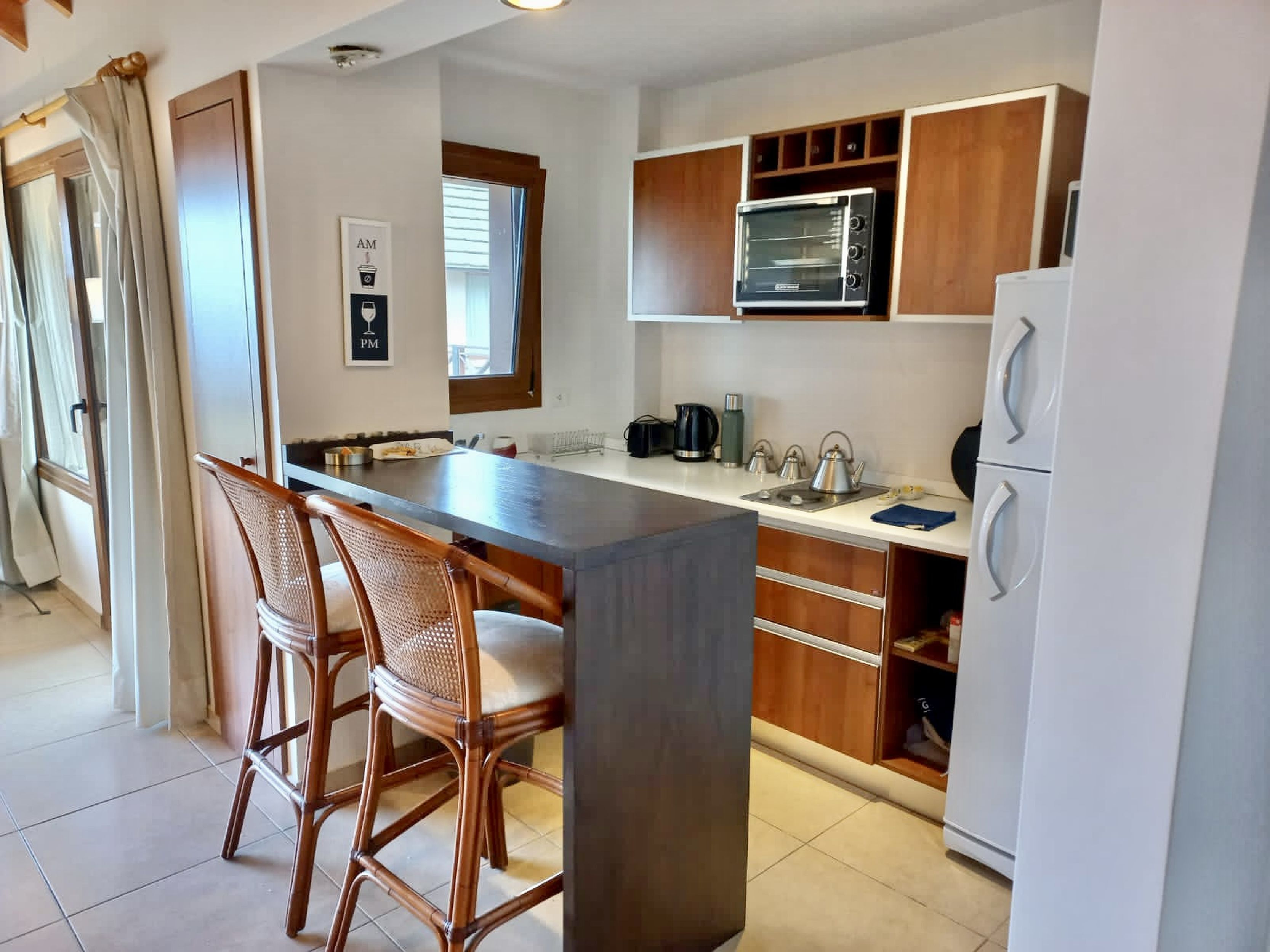 A modern kitchen with a central island, wooden cabinets, a microwave, and a refrigerator.