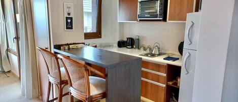 A modern kitchen with a central island, wooden cabinets, a microwave, and a refrigerator.