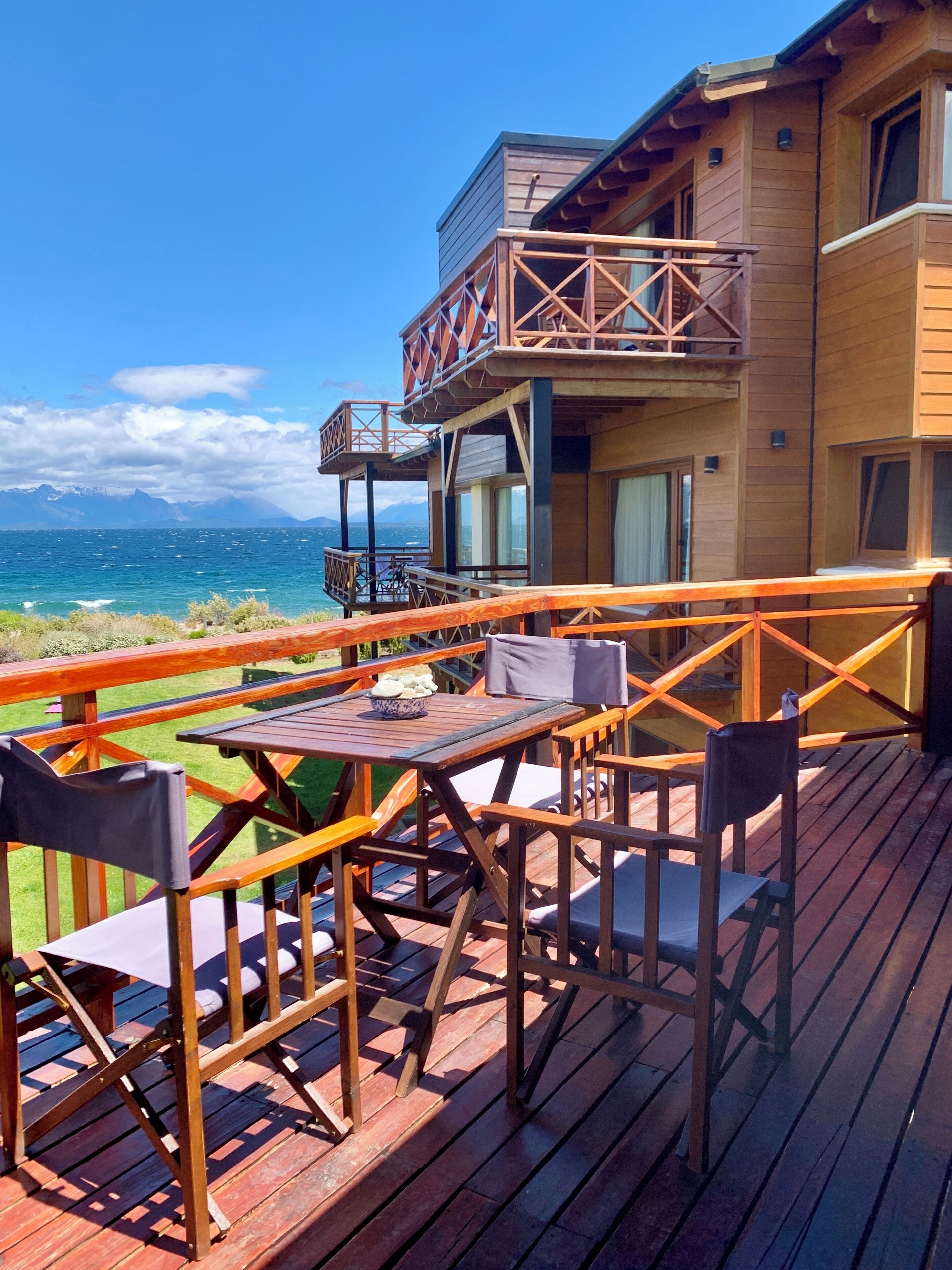 Eine Holzterrasse mit Sitzgelegenheiten im Freien, mit Blick auf ein Gewässer und Berge.