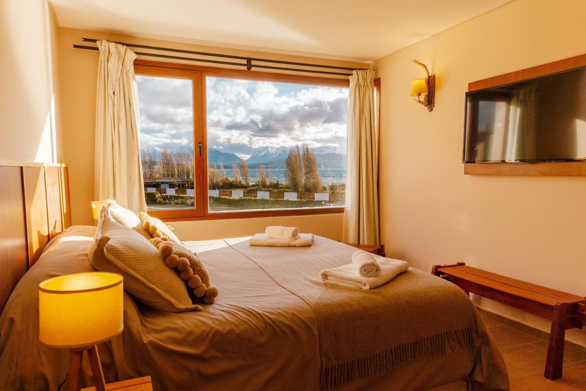 Una habitación de hotel con una cama, una lámpara de noche, un televisor y una ventana con vistas a la montaña.