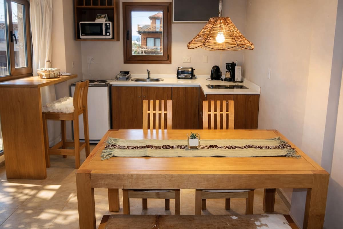 Cocina compacta con armarios de madera, microondas y comedor con mesa y sillas.