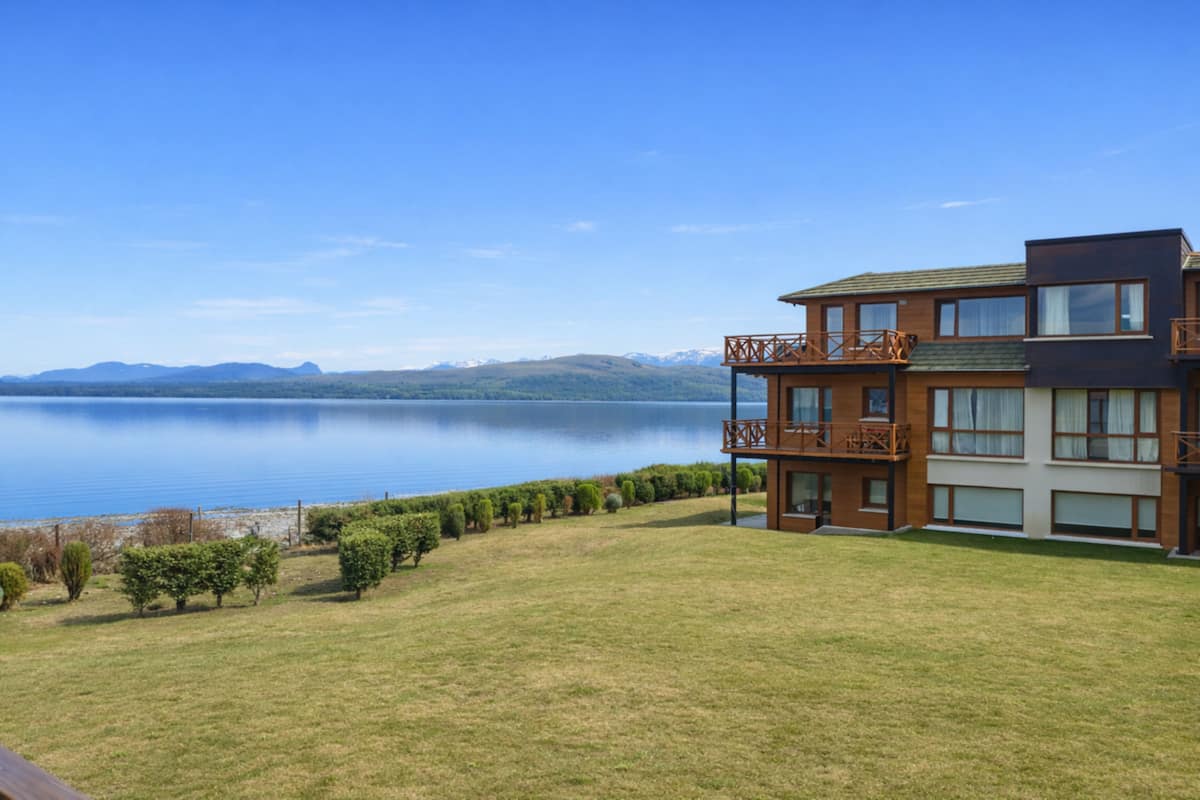Un edificio moderno de dos pisos con un balcón, un césped y vista al lago.