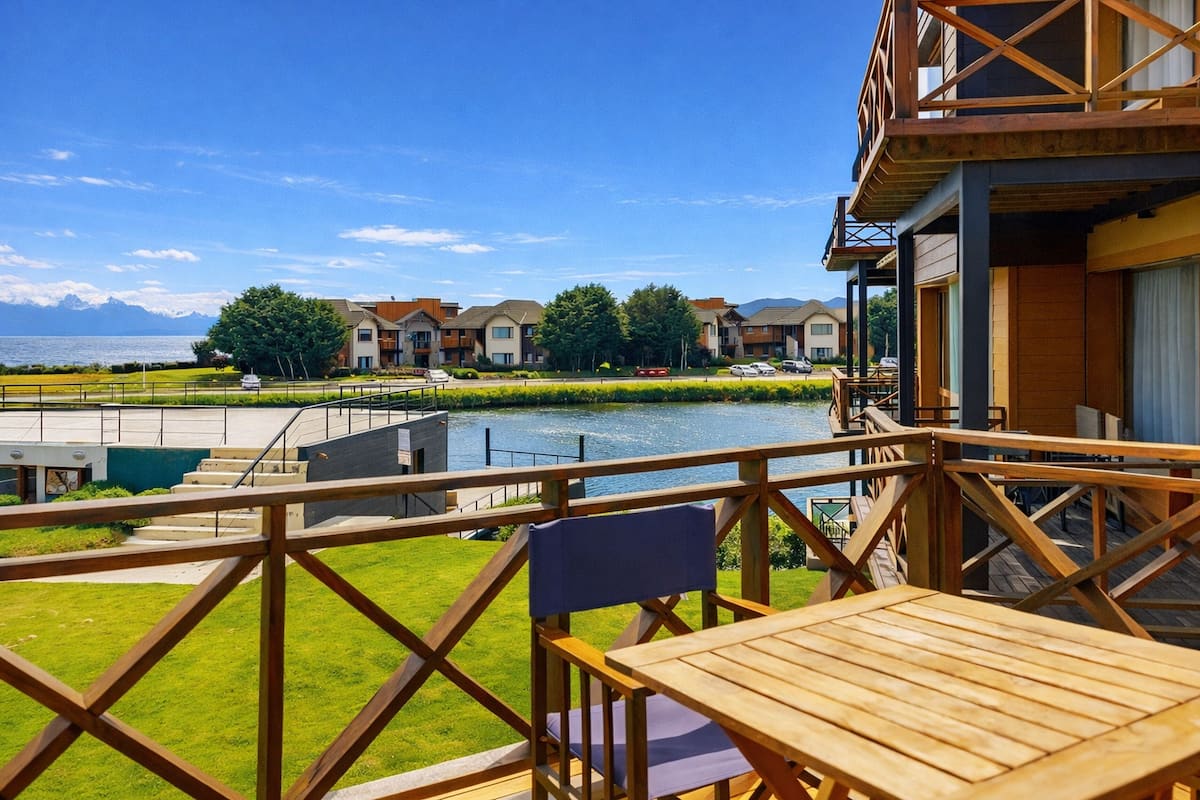 Una terraza de madera con una mesa y una silla, con vistas a un cuerpo de agua y edificios.