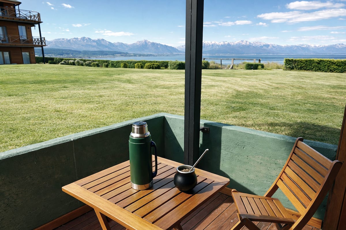 Un patio con una mesa, un termo y una taza, con vistas a una zona cubierta de césped y montañas a lo lejos.