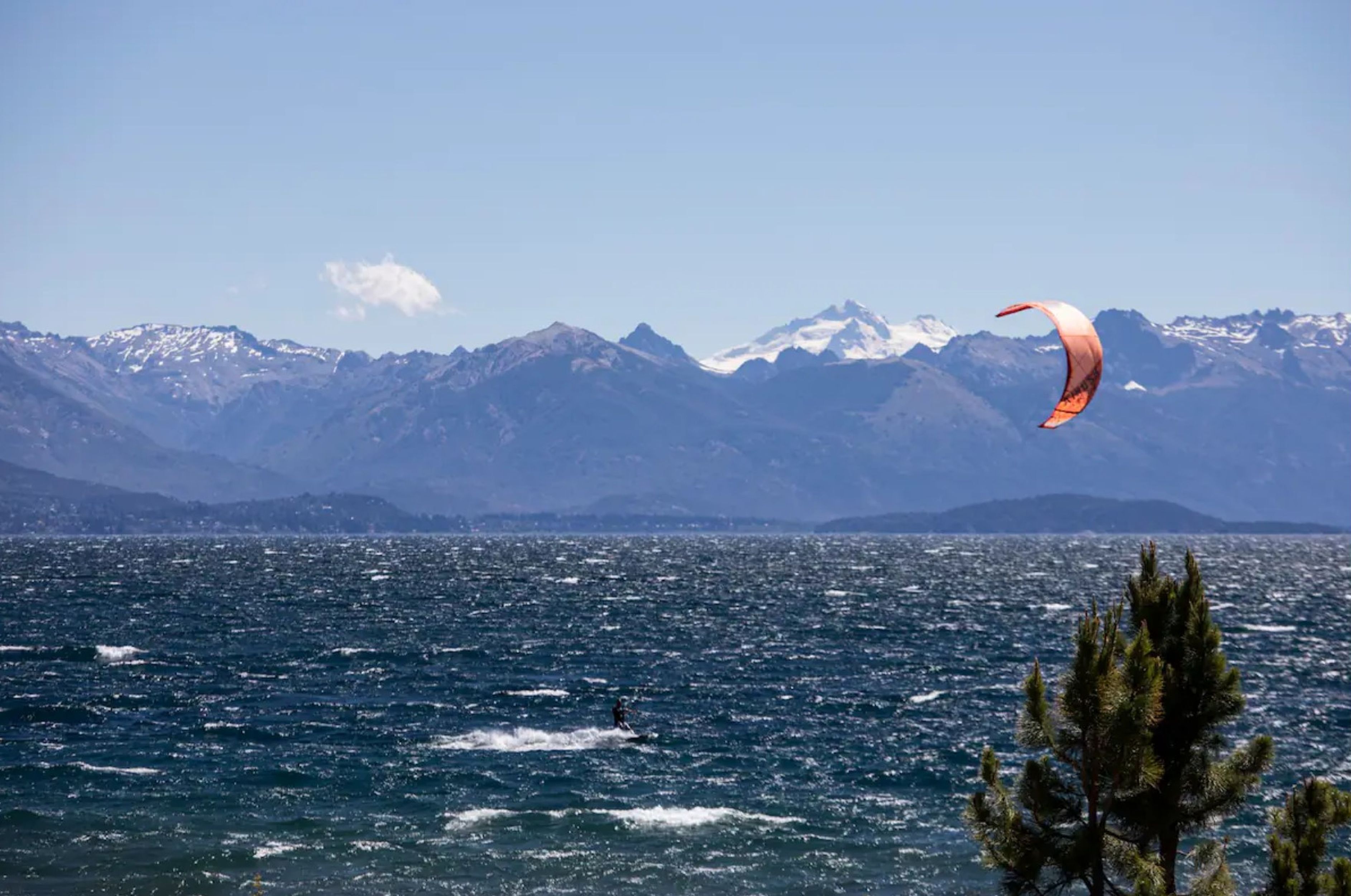 A lake with a person kite surfing, surrounded by mountains.