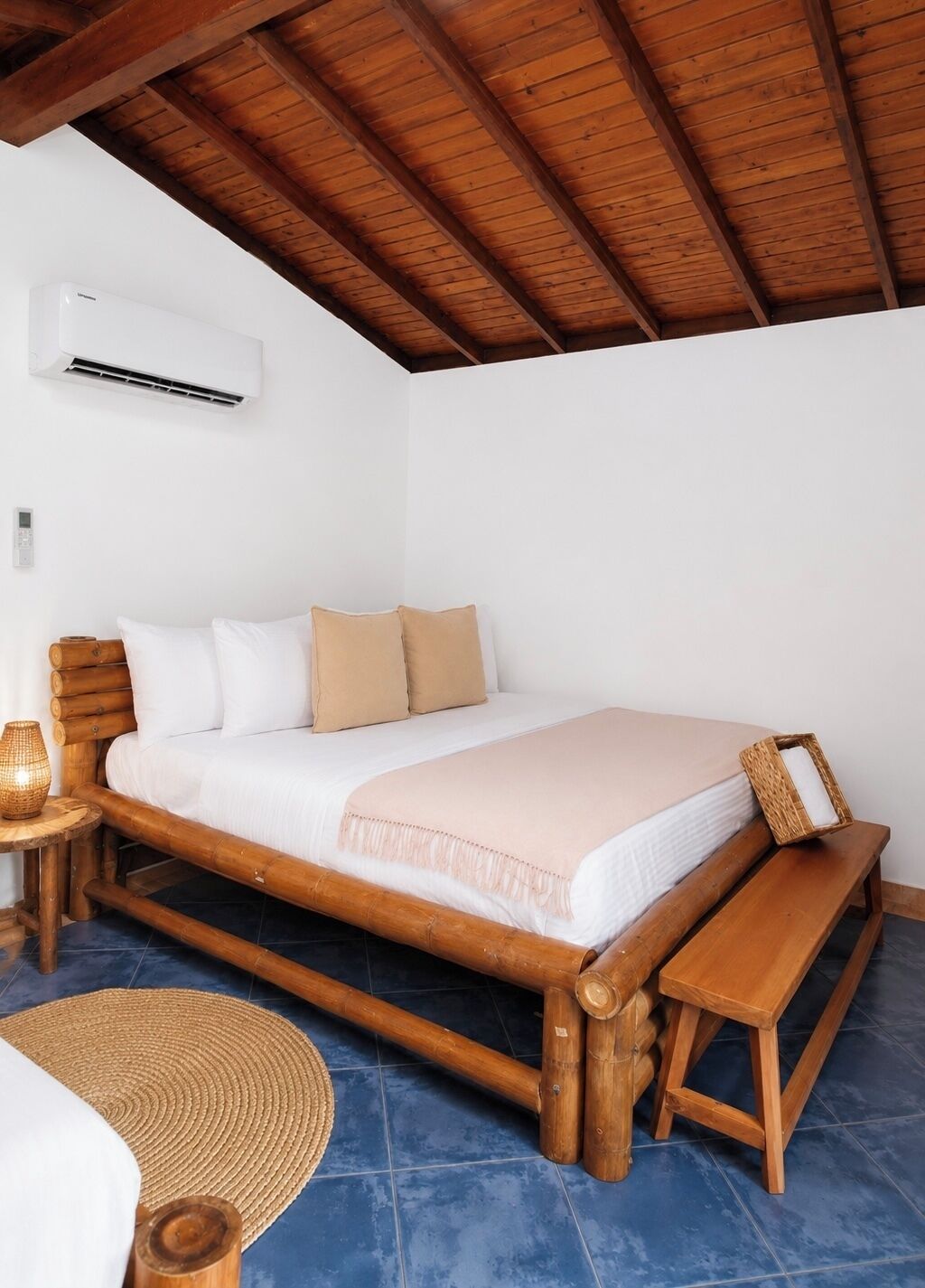 A wooden bed with a bench, a bedside table, a woven mat, and an air conditioning unit.
