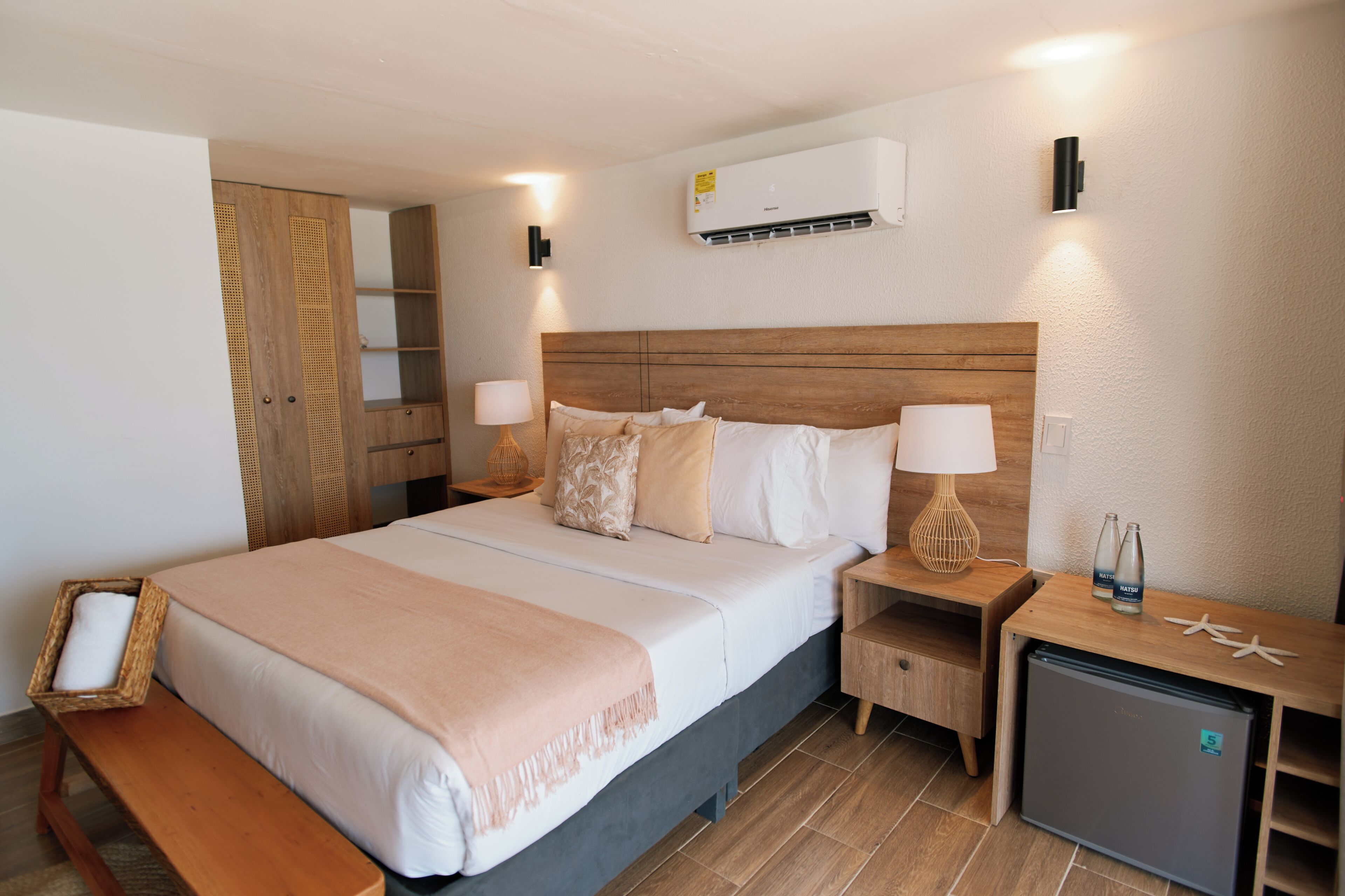 A hotel room with a bed, bedside tables, a small refrigerator, and a wardrobe.