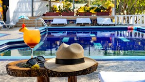 A poolside setting with a hat, sunglasses, and a drink on a wooden table.