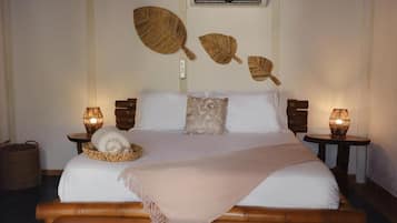A neatly made bed with a white comforter, two pillows, a woven basket with towels, and two bedside lamps on wooden nightstands.