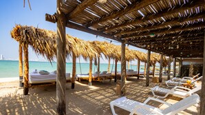 A beachside lounge area with thatched umbrellas, white lounge chairs, and a view of the sea.
