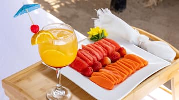 Una bandeja con un vaso de jugo de naranja, una rodaja de naranja, una cereza y una pajita, junto a un plato de sandía en rodajas, fresas y melón.