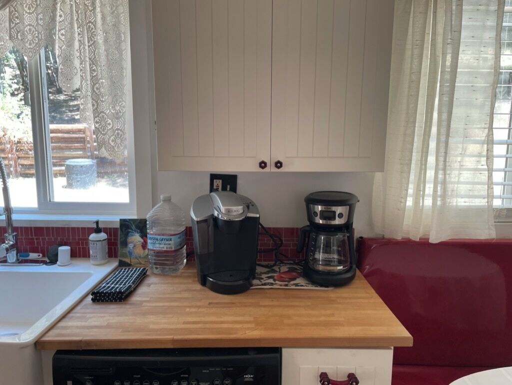 A kitchen with a wooden countertop, a coffee maker, a water dispenser, and a dishwasher.